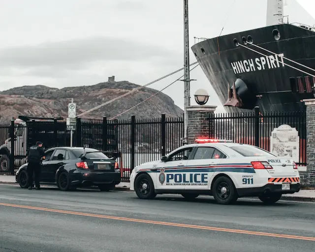 Vehículos policiales estacionados cerca del barco Hinch Spirit en un entorno urbano, con un enfoque en la seguridad pública y la vigilancia.