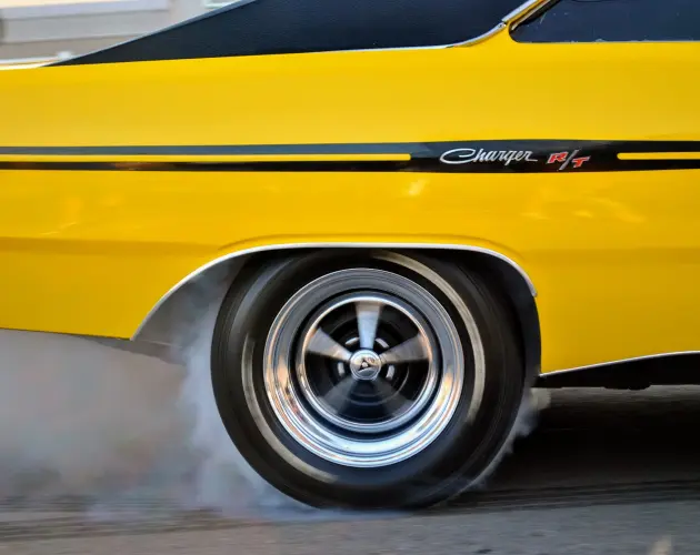 Dodge Charger R/T amarillo con llantas brillantes y humo saliendo de las ruedas traseras, mostrando potencia y velocidad.