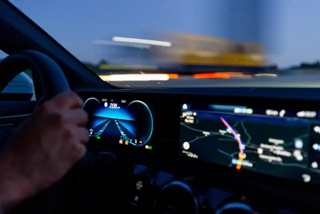 Interior view of a car dashboard at night, showing speedometer and navigation screen with illuminated controls.