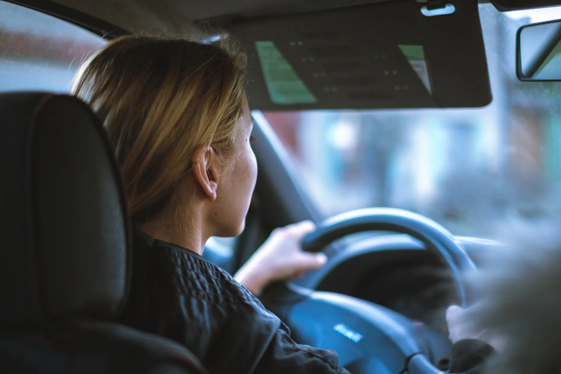 A woman with blonde hair driving a car, focusing on the steering wheel and dashboard, showcasing a modern vehicle interior.